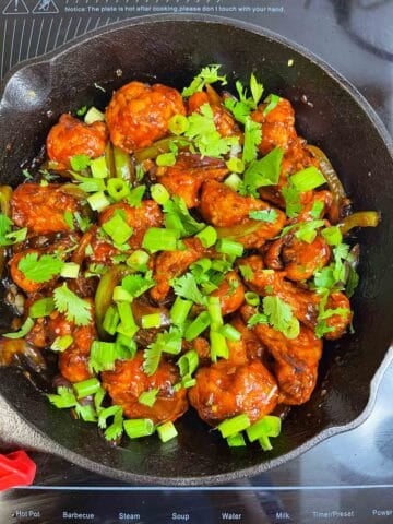 dry gobi manchurian served in a iron skillet garnished with cilantro and green onions