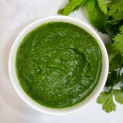 green chutney served in a bowl with mint and coriander leaves on the side