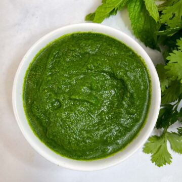 green chutney served in a bowl with mint and coriander leaves on the side
