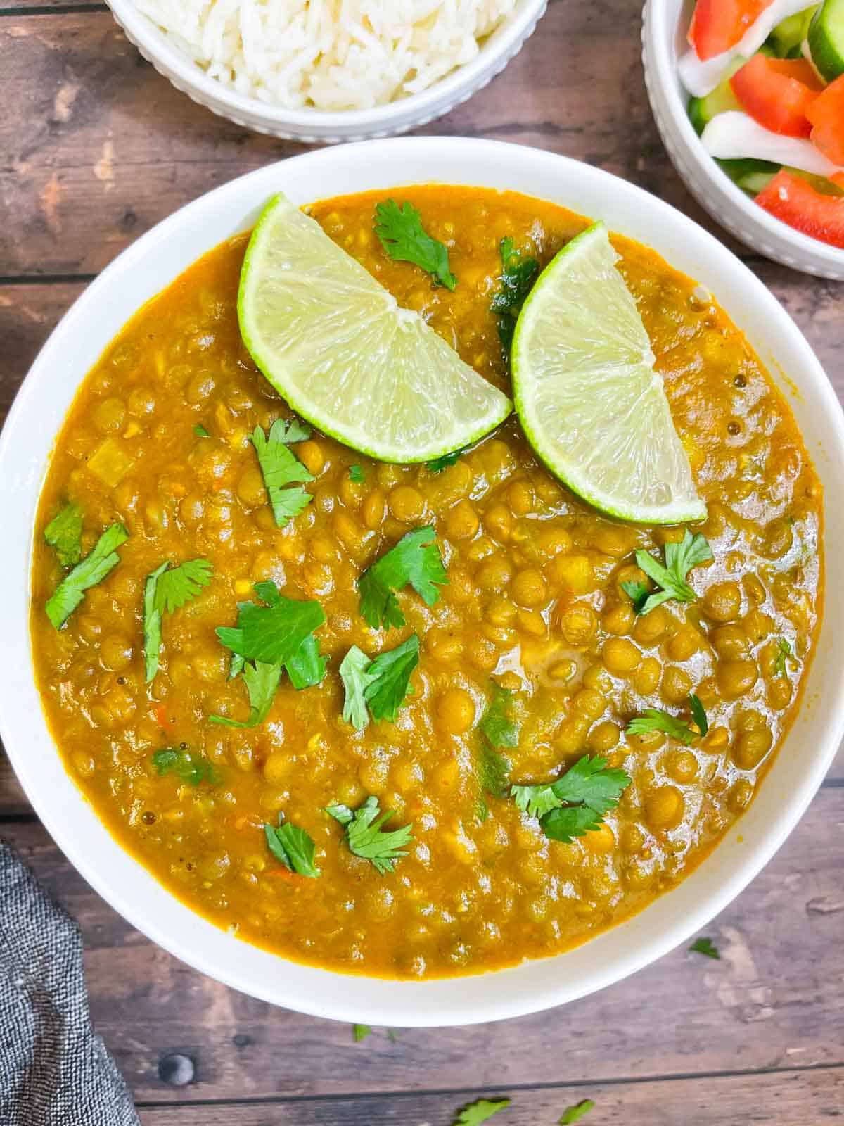 whole masoor dal recipe served in a bowl garnished with lemon wedges and cilantro with a spoon 