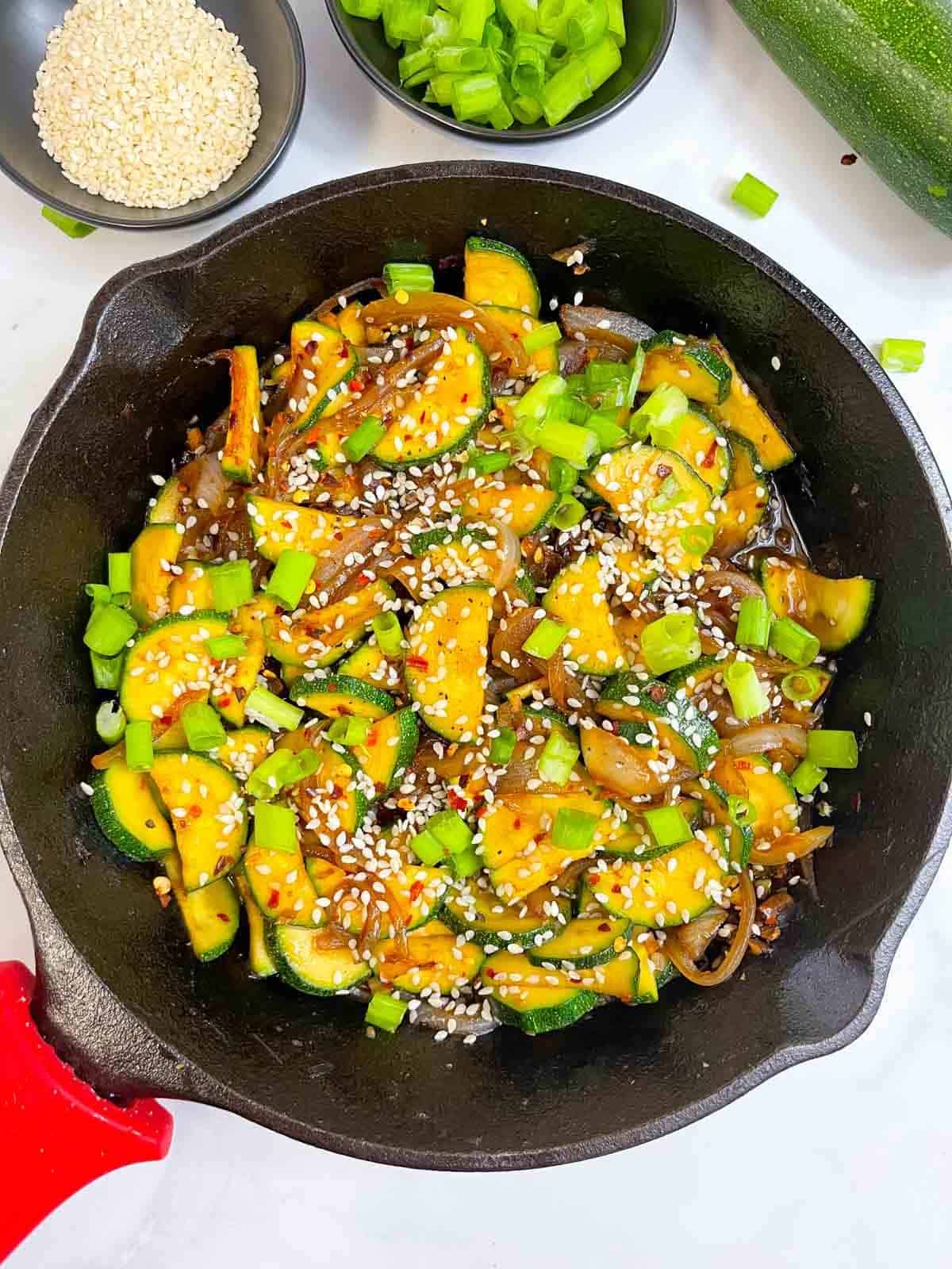 asian style zucchini stir fry served garnished with sesame seeds with spring onions on the side