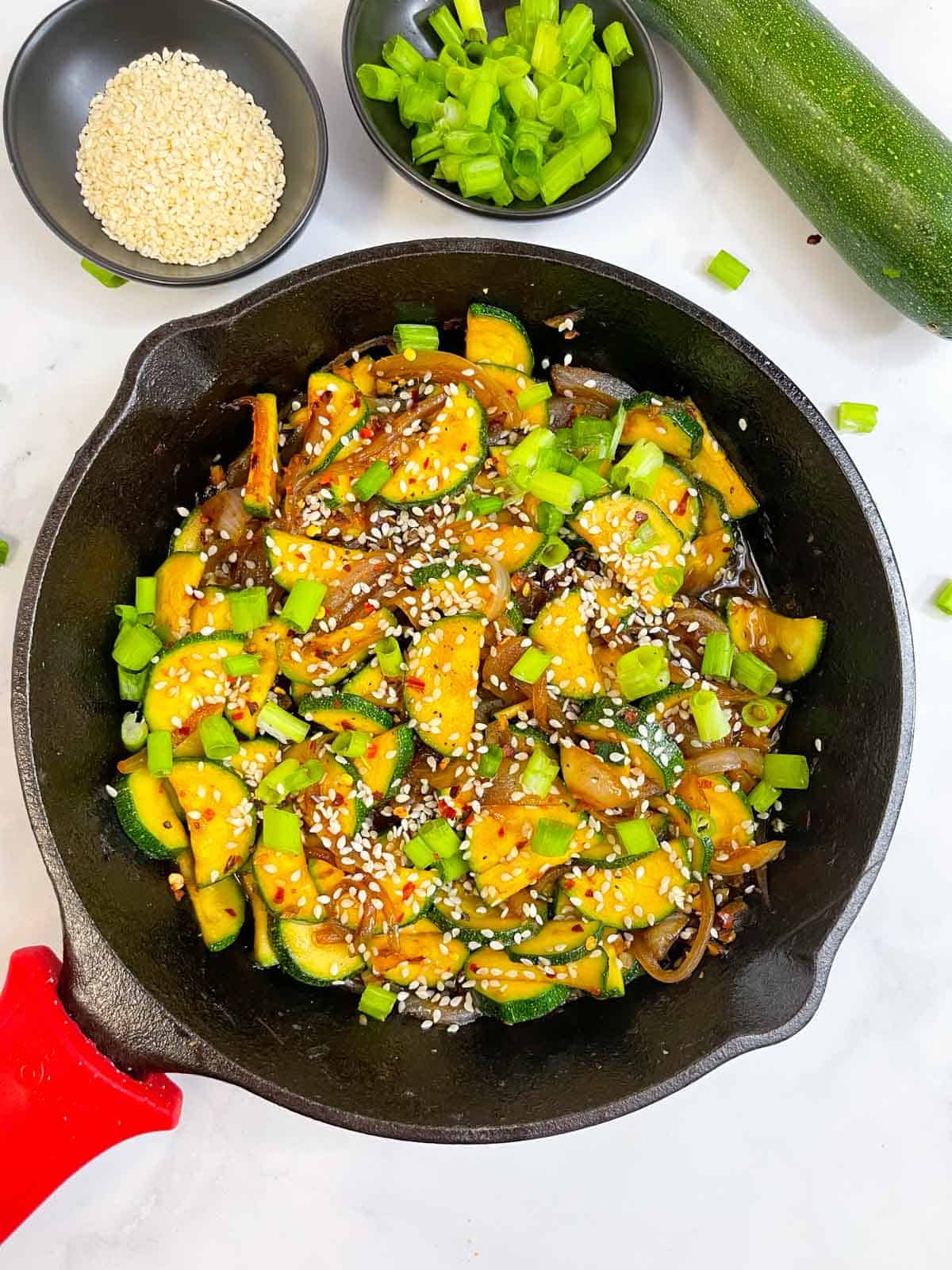zucchini stir fry served on a skillet garnished with green onions and toasted sesame seeds