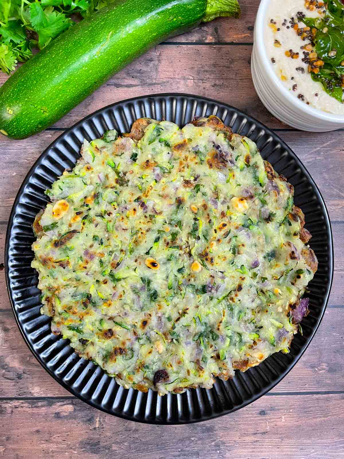 zucchini thalipettu served on a plate with coconut chutney on the side