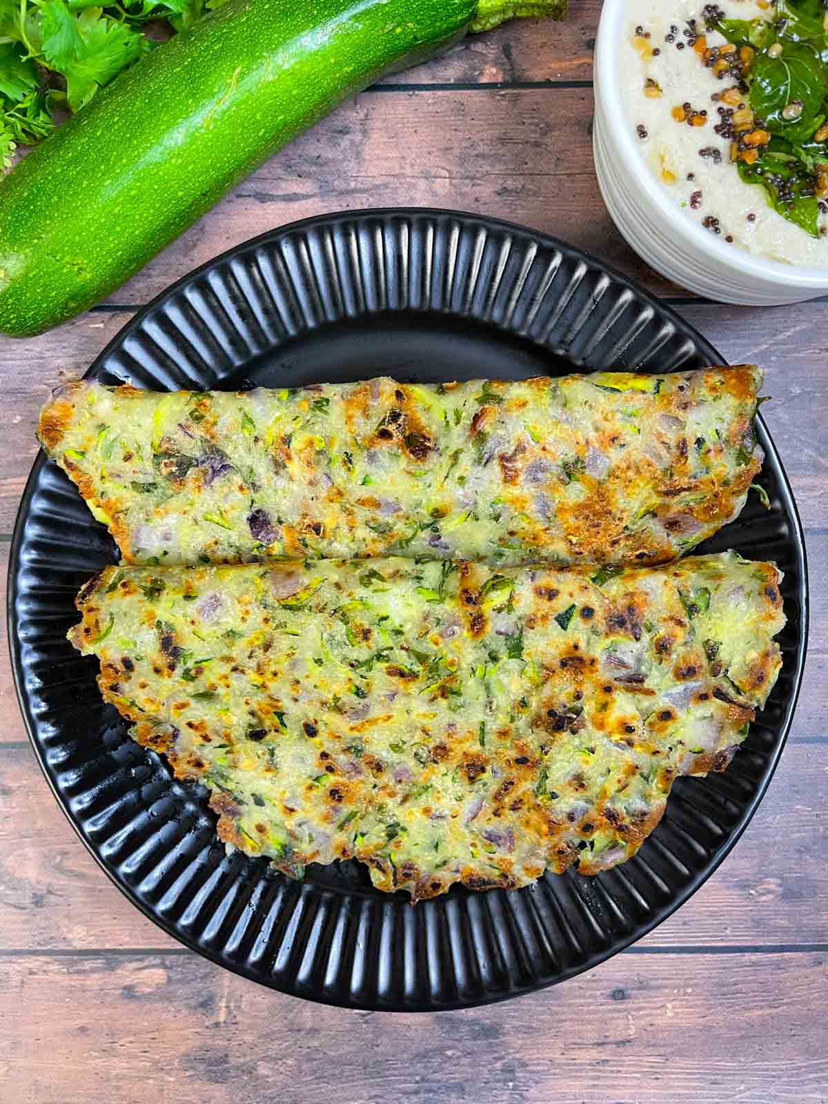 zucchini thalipettu served on a plate with coconut chutney on the side