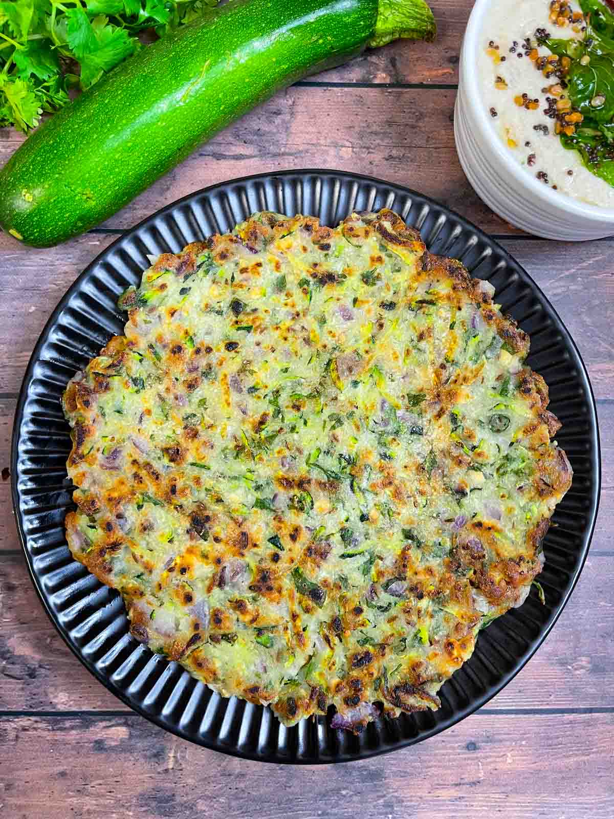 zucchini thalipettu served on a plate with coconut chutney on the side