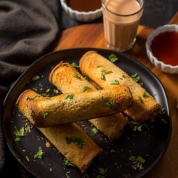 Bread rolls served on a plate with chutneys and chai on the side.