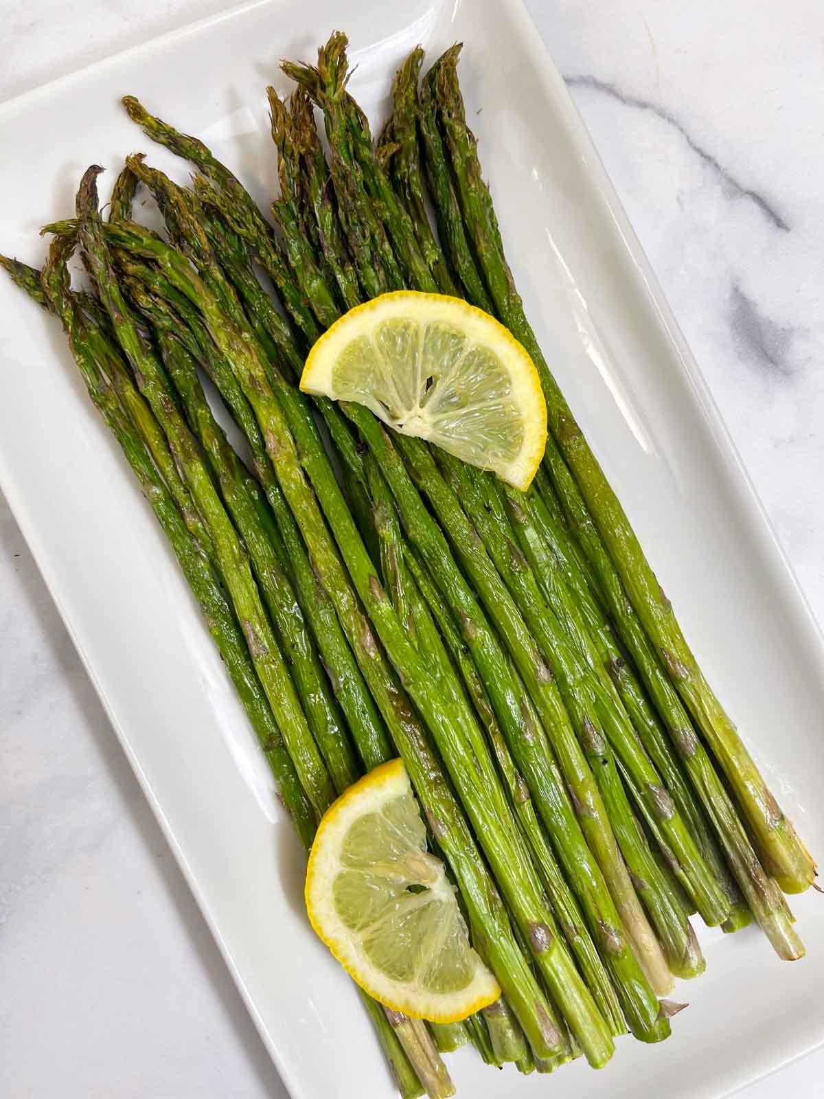 roasted air fryer asparagus served on a plate with two lemon wedges