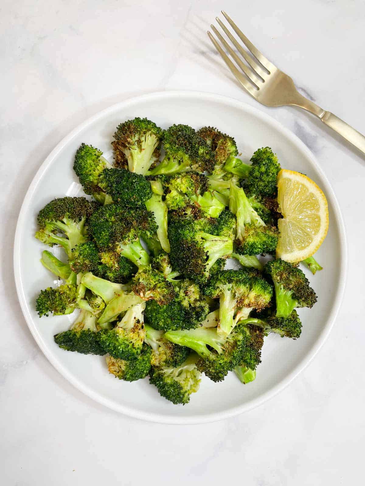 air fryer roasted broccoli served on a plate with lemon wedge on the side.