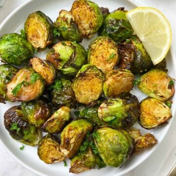 roasted brussels sprouts served in a plate with lemon wedge on the side and garnished with parsley