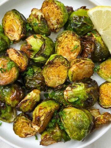 roasted brussels sprouts served in a plate with lemon wedge on the side and garnished with parsley