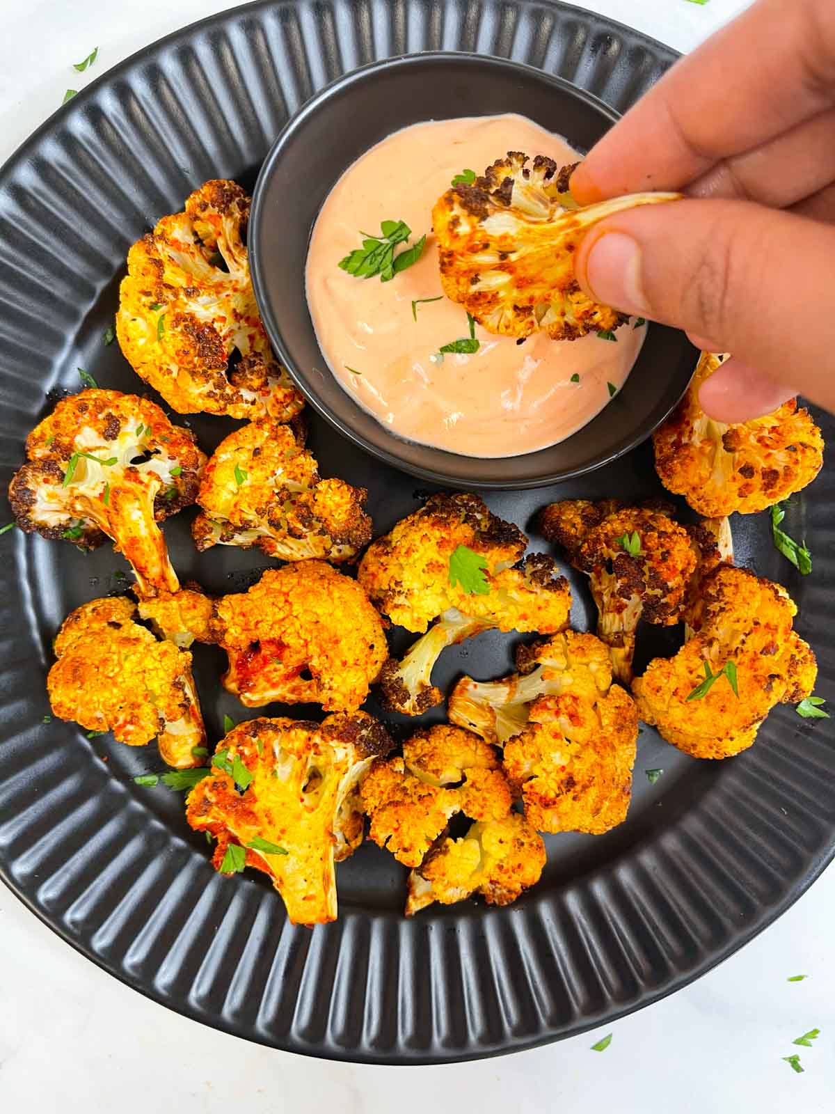 Dipping a roasted cauliflower into the sauce with the other roasted cauliflowers on the plate