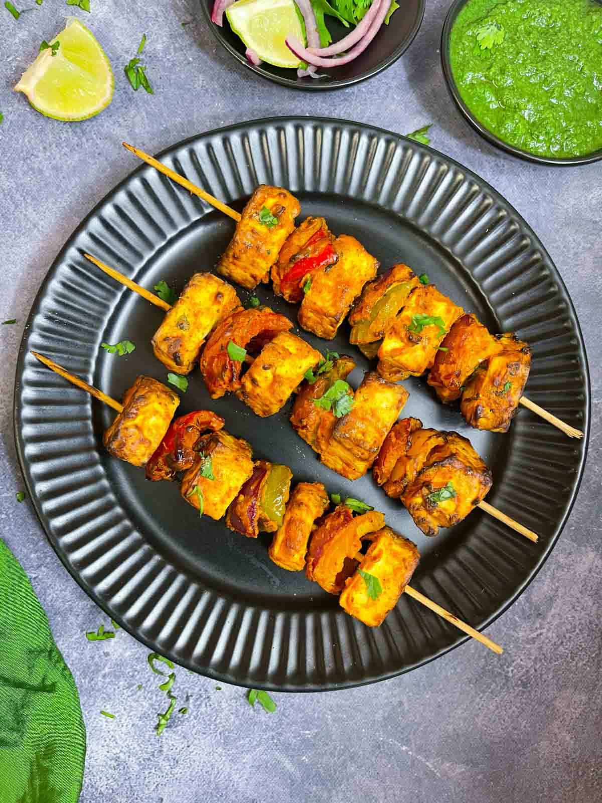 tandoori paneer tikka prepared in air fryer lined on a plate with green chutney , lemon and onions on the side