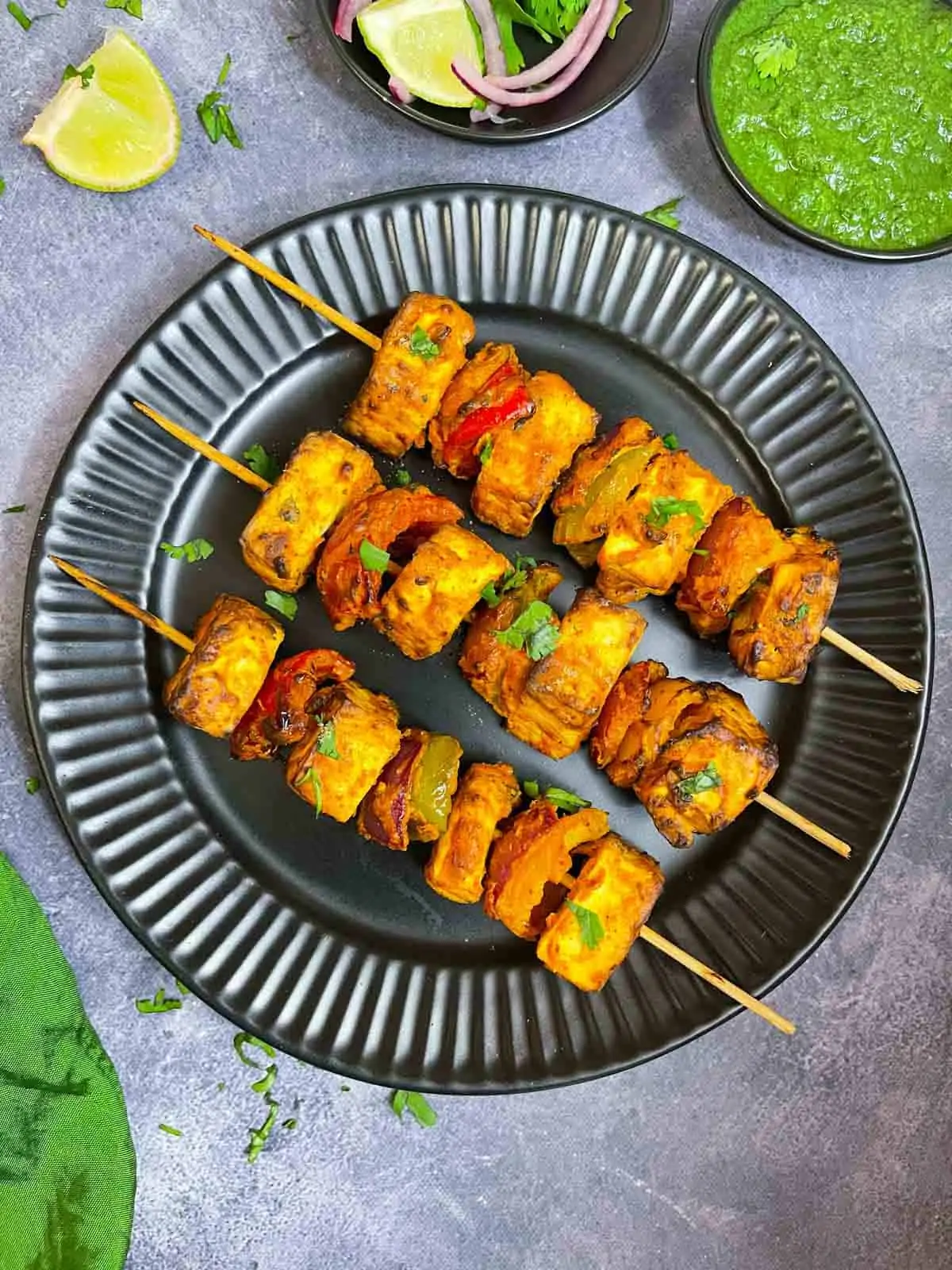 tandoori paneer tikka prepared in air fryer lined on a plate with green chutney, lemon and onions on the side
