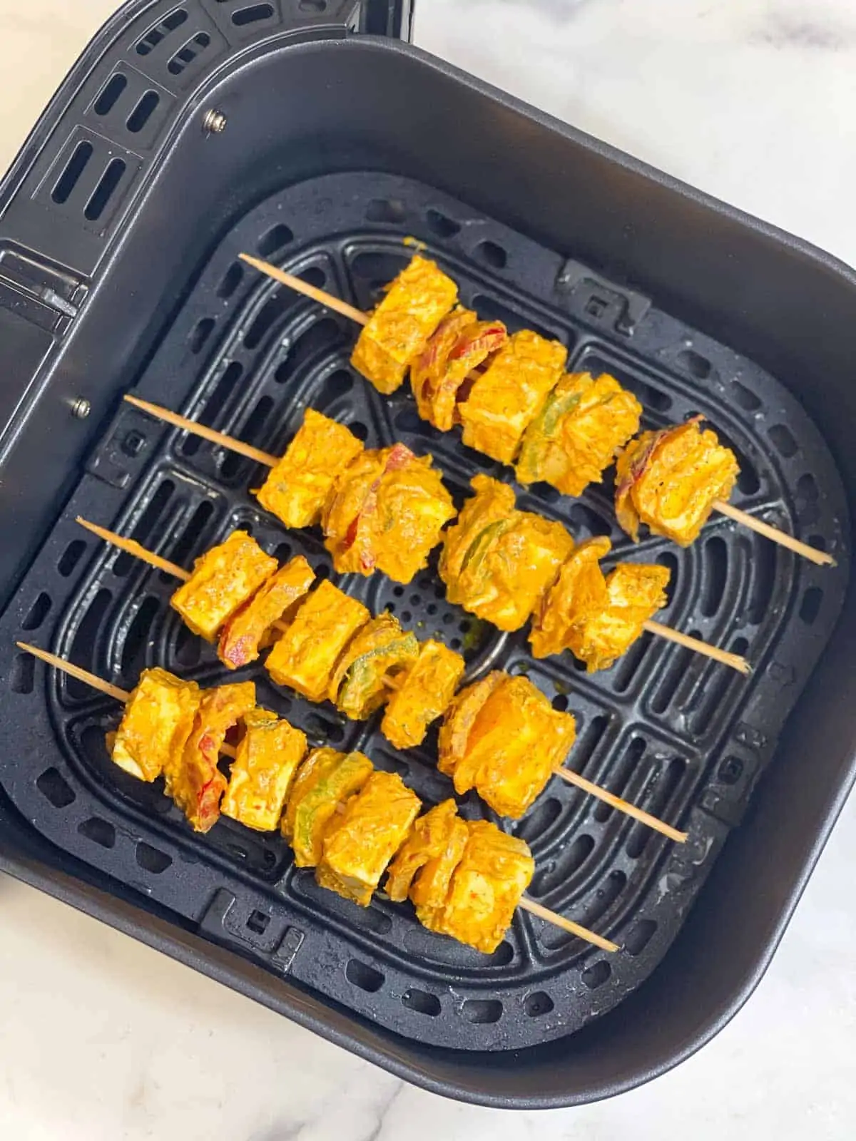 paneer tikka in skewers arranged on a air fryer basket