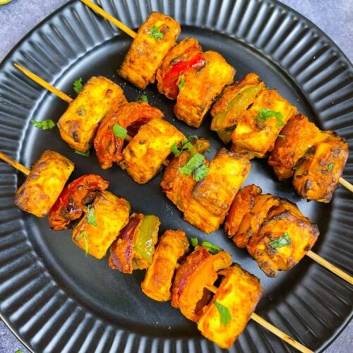 tandoori paneer tikka prepared in air fryer lined on a plate with green chutney , lemon and onions on the side