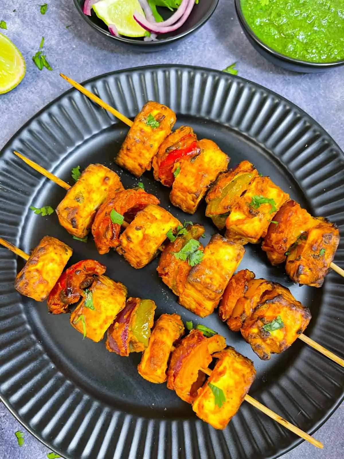 tandoori paneer tikka prepared in air fryer lined on a plate with green chutney , lemon and onions on the side
