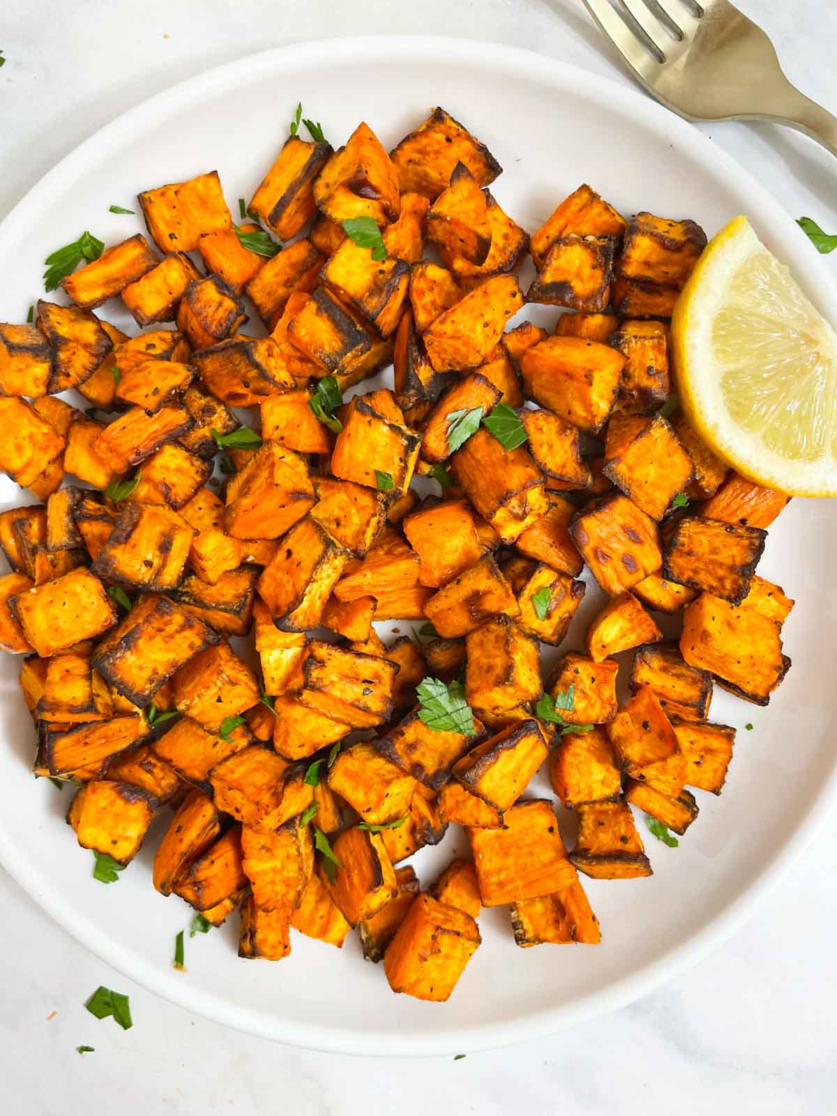 air fryer roasted sweet potato cubes served on a plate garnished with cilantro with lemon wedge on the side