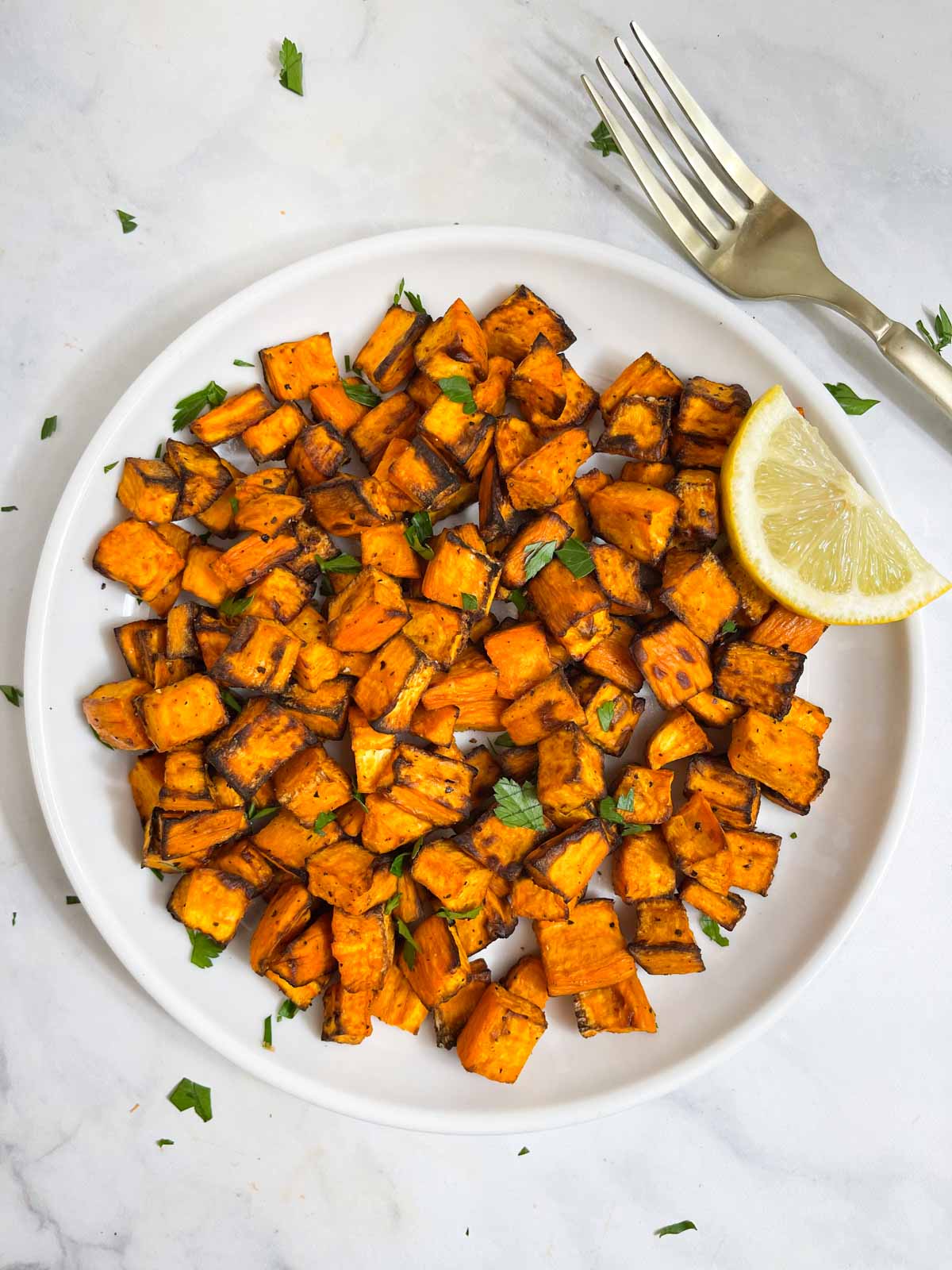 air fried sweet potato served on a plate with a lemon wedge and fork on the side