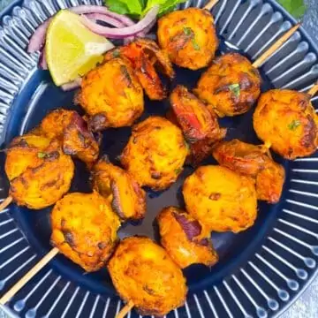 tandoori aloo served on a plate with lemon wedges and onion