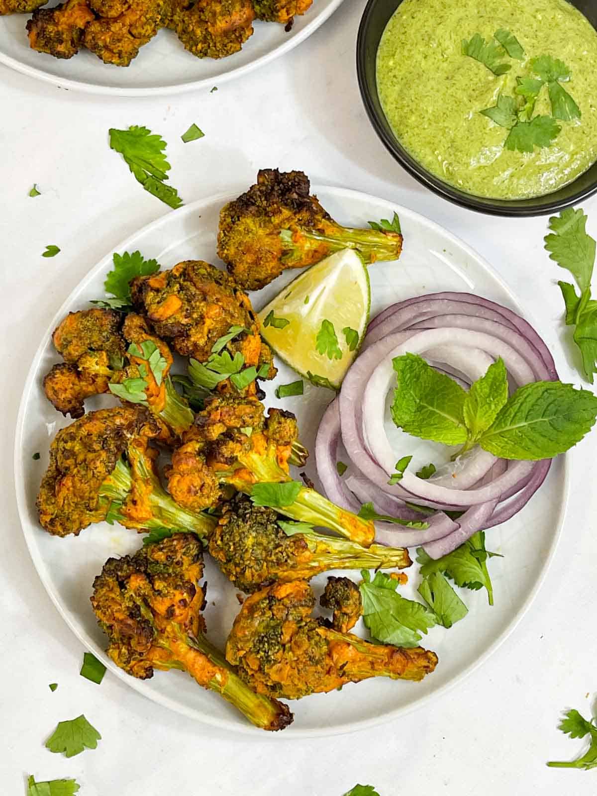 tandoori broccoli tikka served on a plate with lime wedge, onions and mint chutney collage