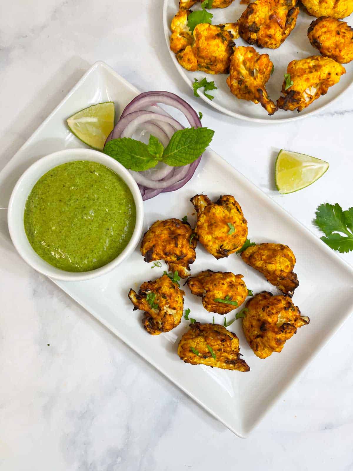 air fryer tikka bites served in a plate with green chutney with lemon wedges and green onion on the side