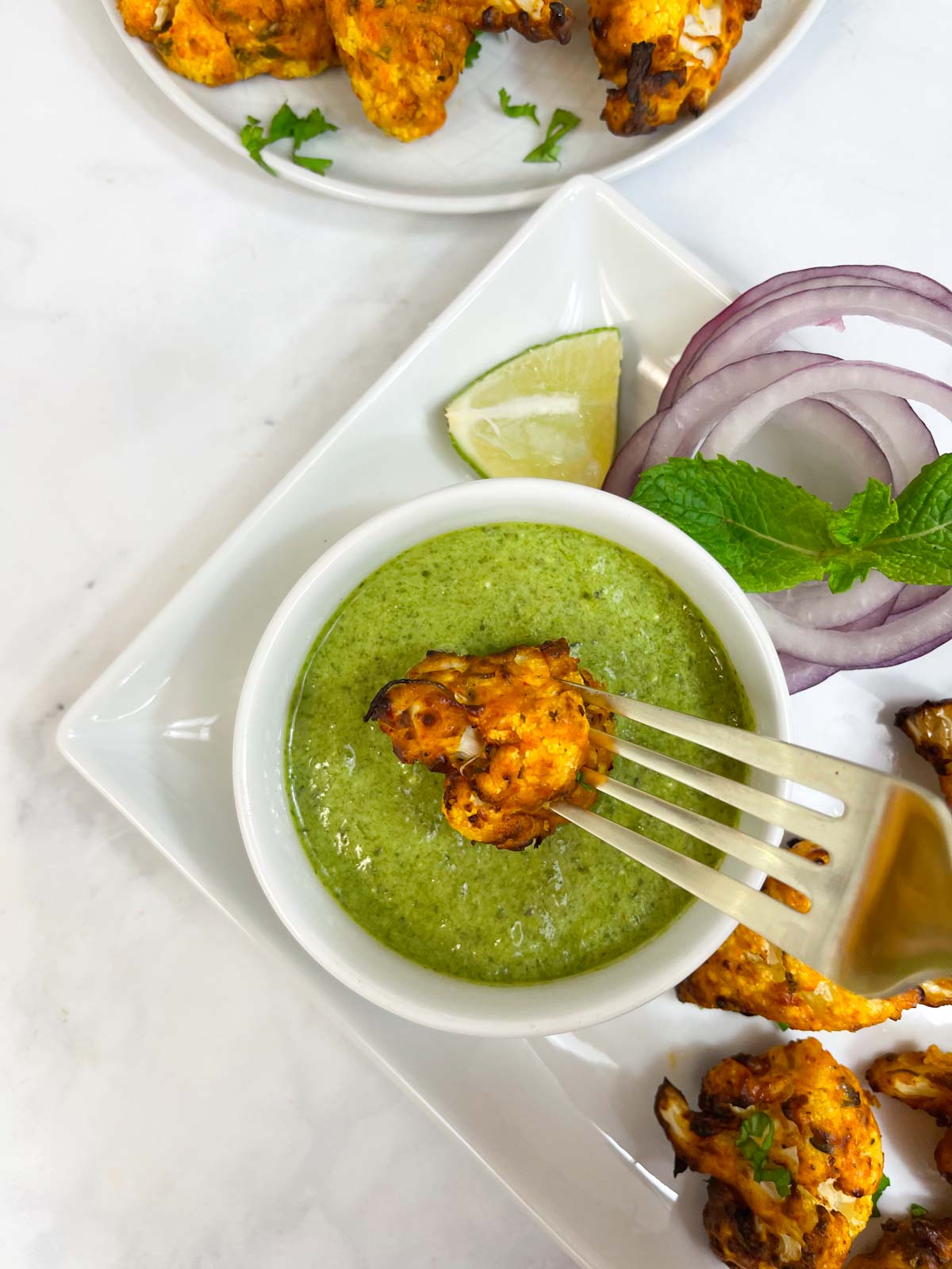 air fryer gobi (cauliflower tikka bites) recipe dipped in cilantro mint chutney using a fork