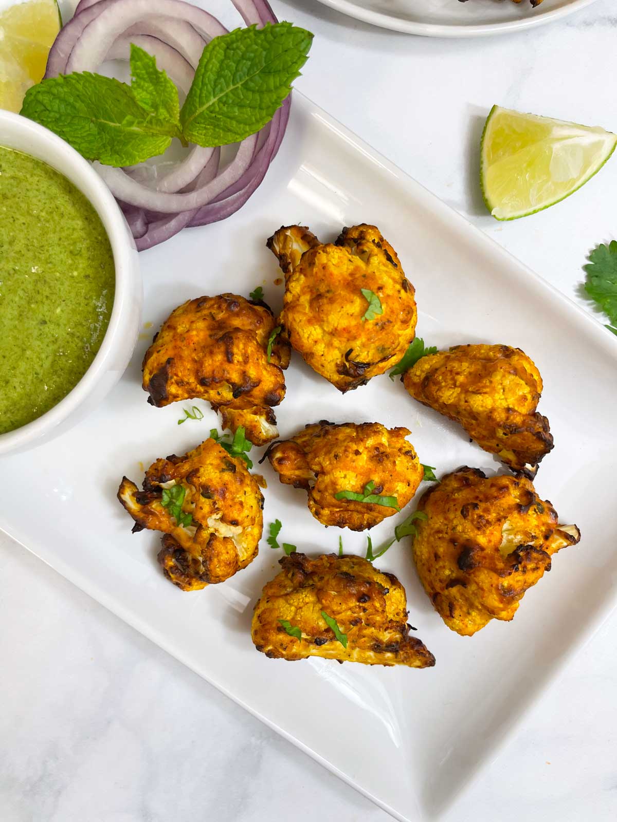 air fryer tandoori gobi served on a plate with onions, green chutney and lemon wedges