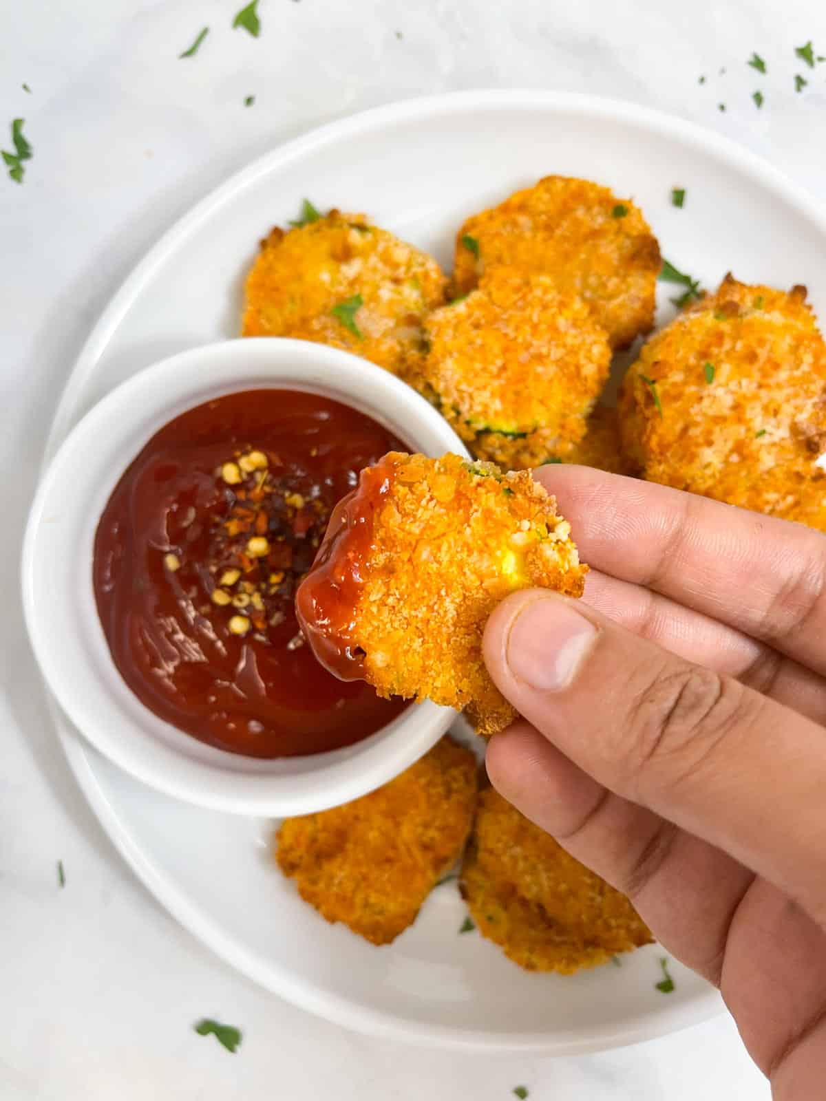 air fryer zucchini dipped in ketchup in hand