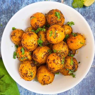 masala aloo served in a bowl garnished with cilantro with lemon wedges on the side