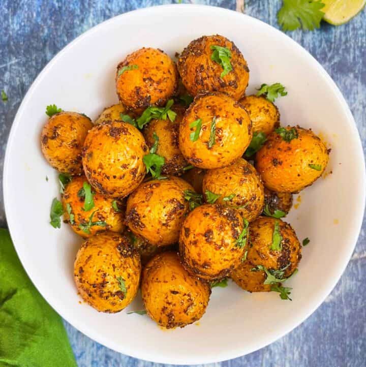 masala aloo served in a bowl garnished with cilantro with lemon wedges on the side