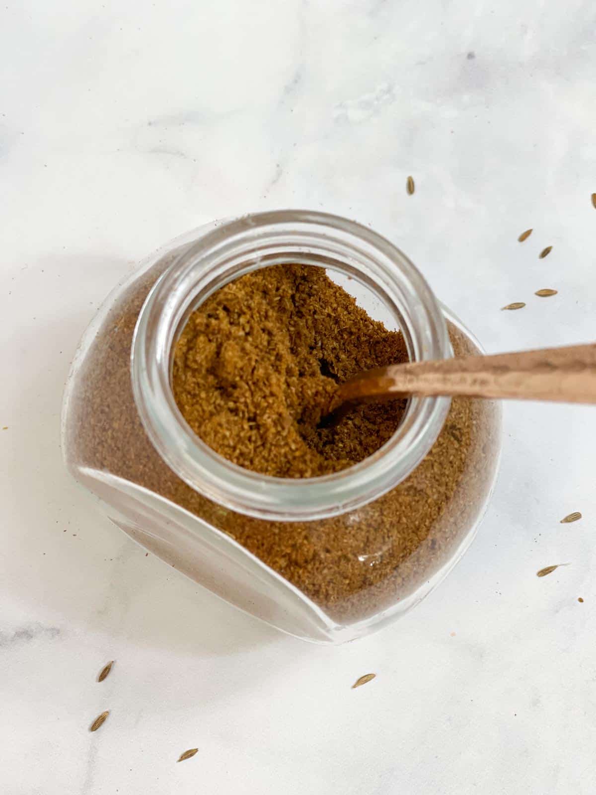 ground cumin powder in a glass container with a spoon