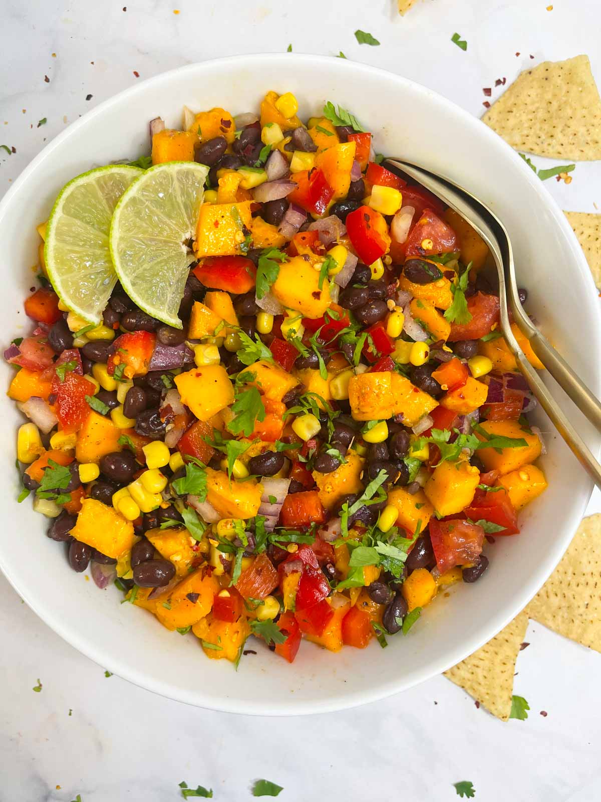 mango black bean salad served in a bowl garnished with cilantro and lime wedges with two spoons