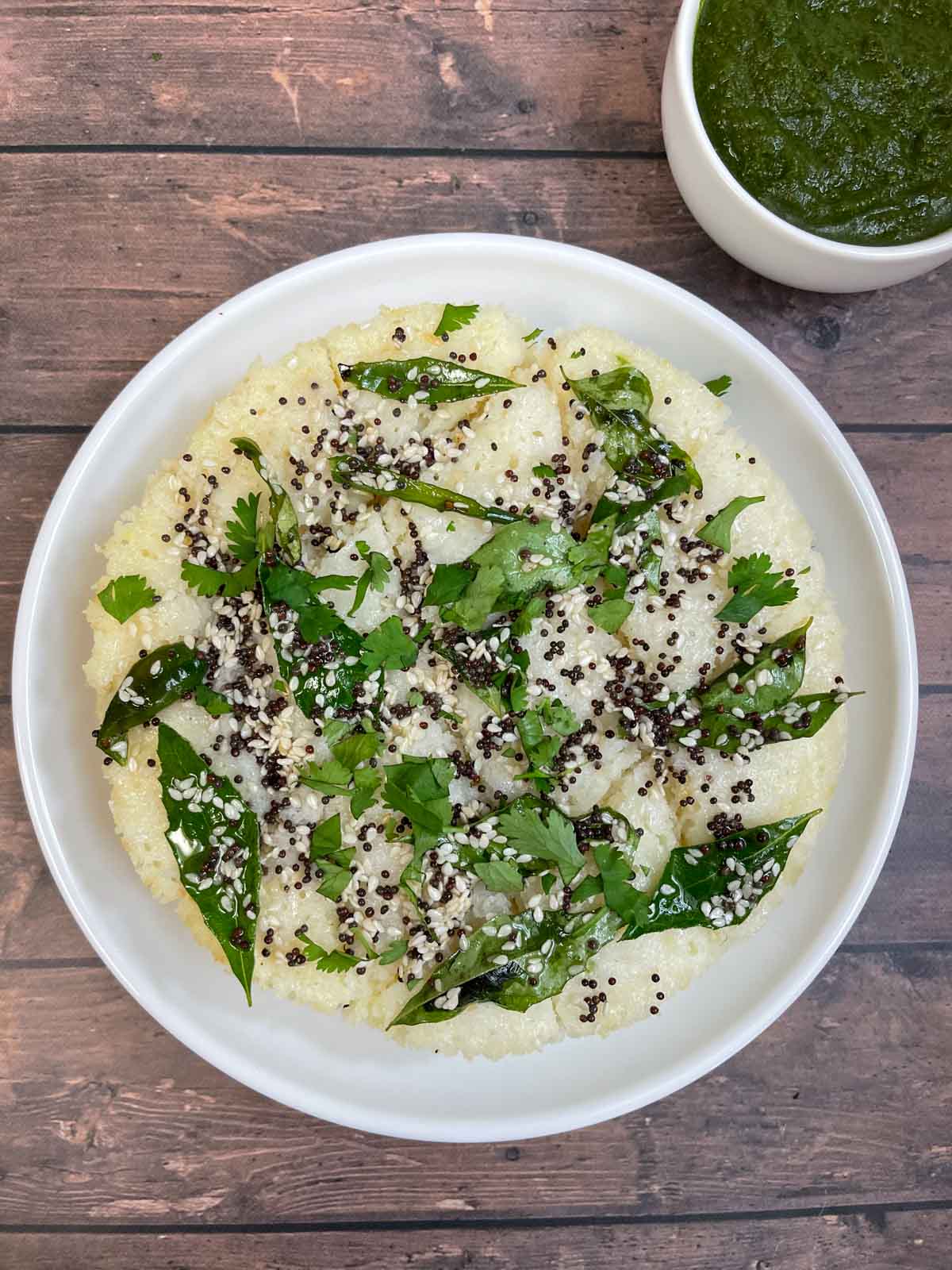 rava dhokla served on a plate garnished with cilantro with green chutney on the side