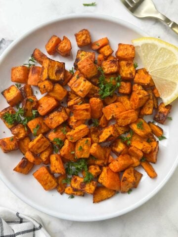 air fryer roasted sweet potatoes served on a plate with lemon wedge on the top