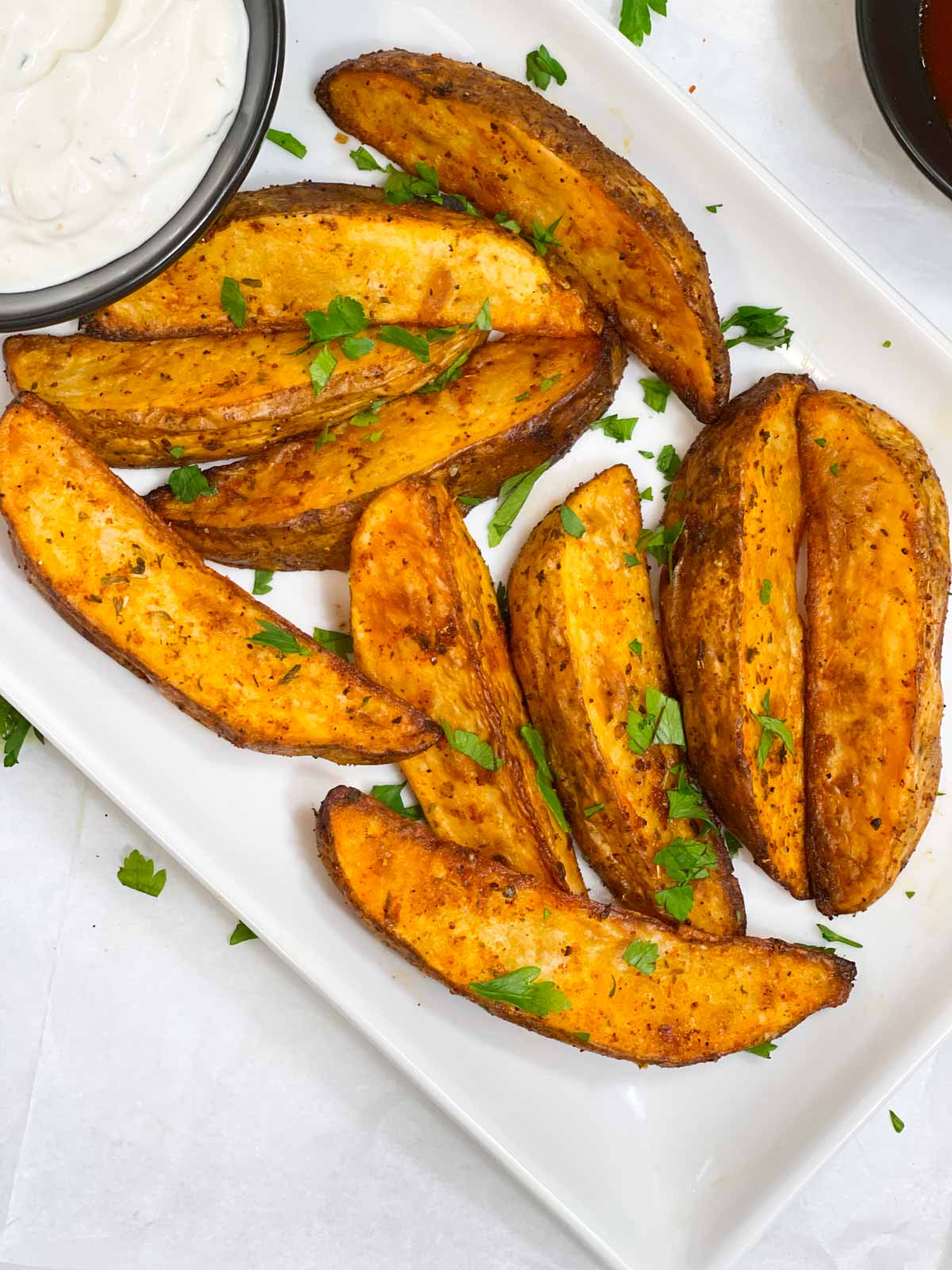 homemade potato wedges on a serving plate garnished with cilantro with a side of dipping sauce