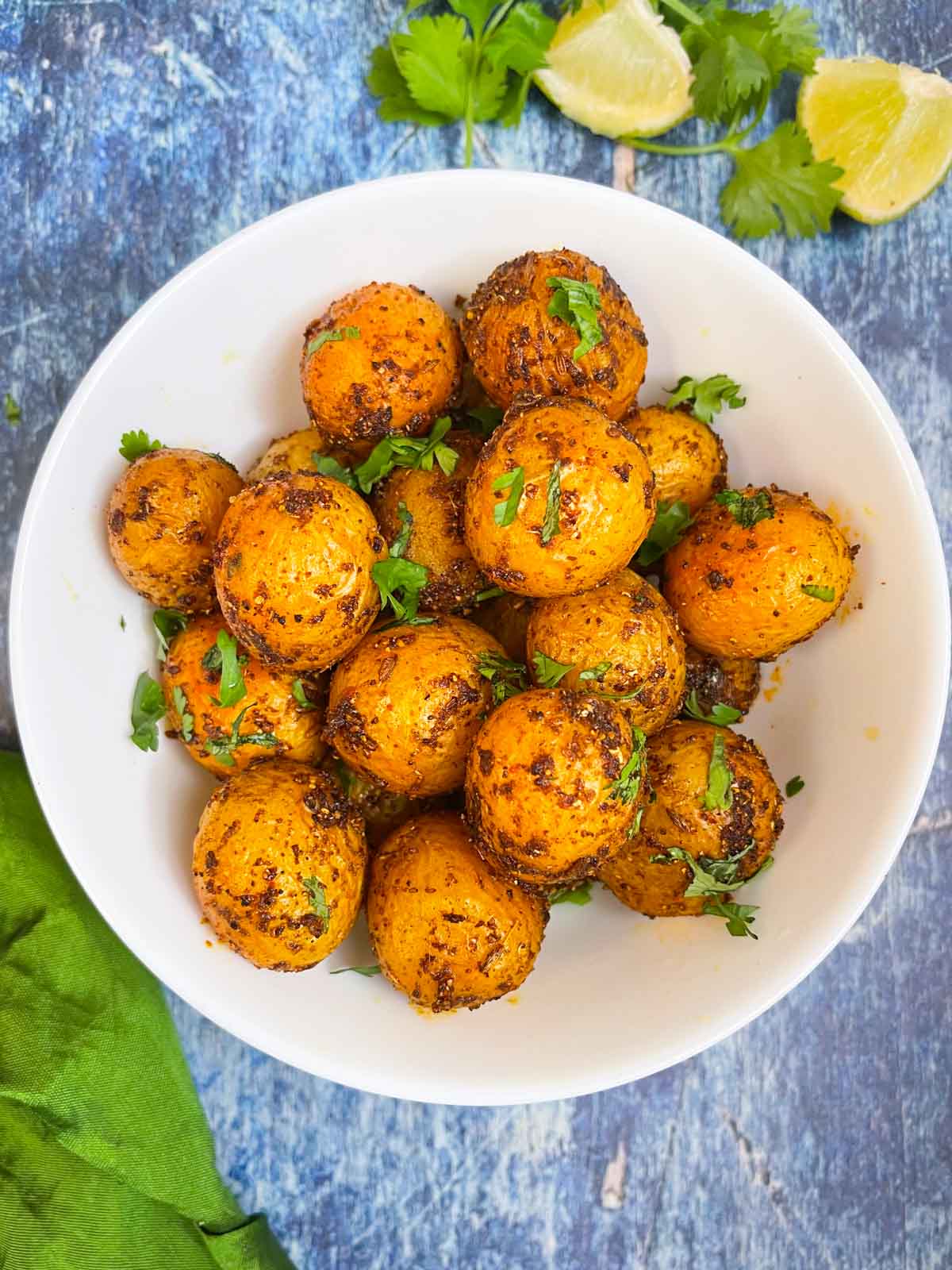 spicy bombay potatoes recipe served in a bowl garnished with cilantro with lemon wedges on the side