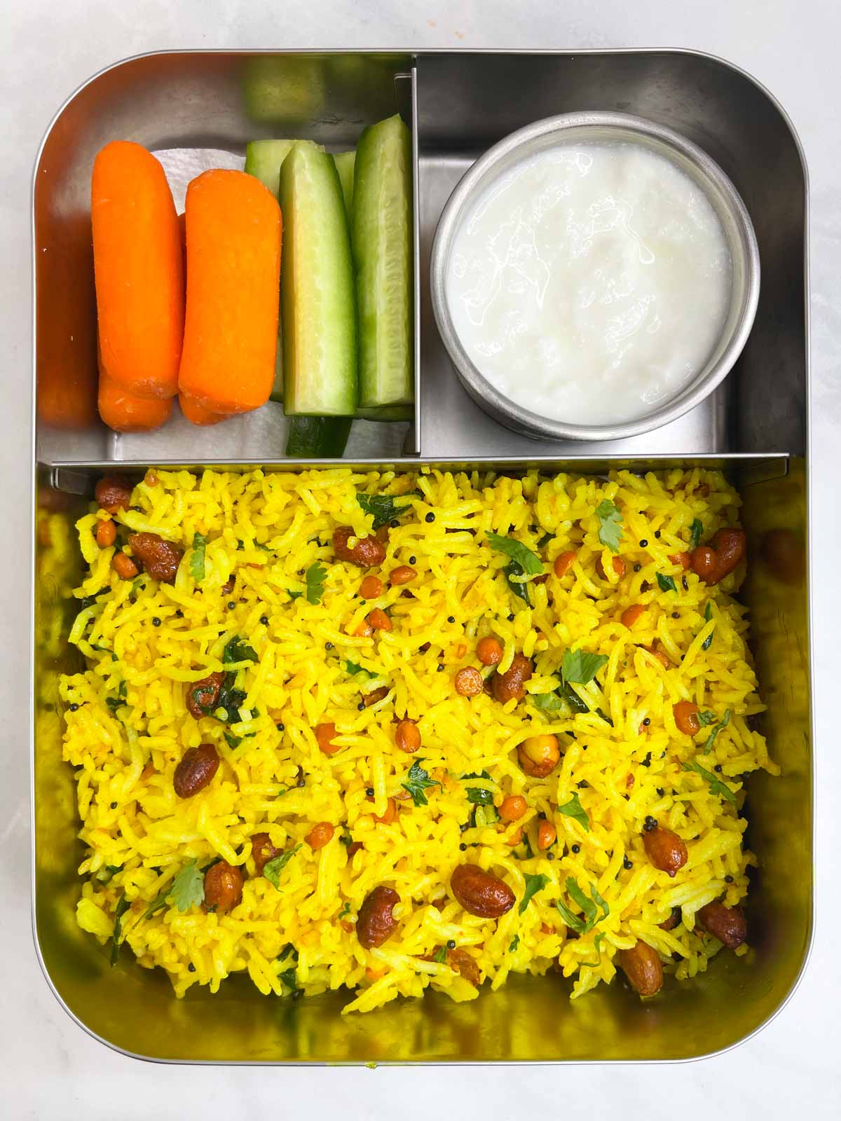 Lemon rice, yogurt and veggies in steel bento lunch box.