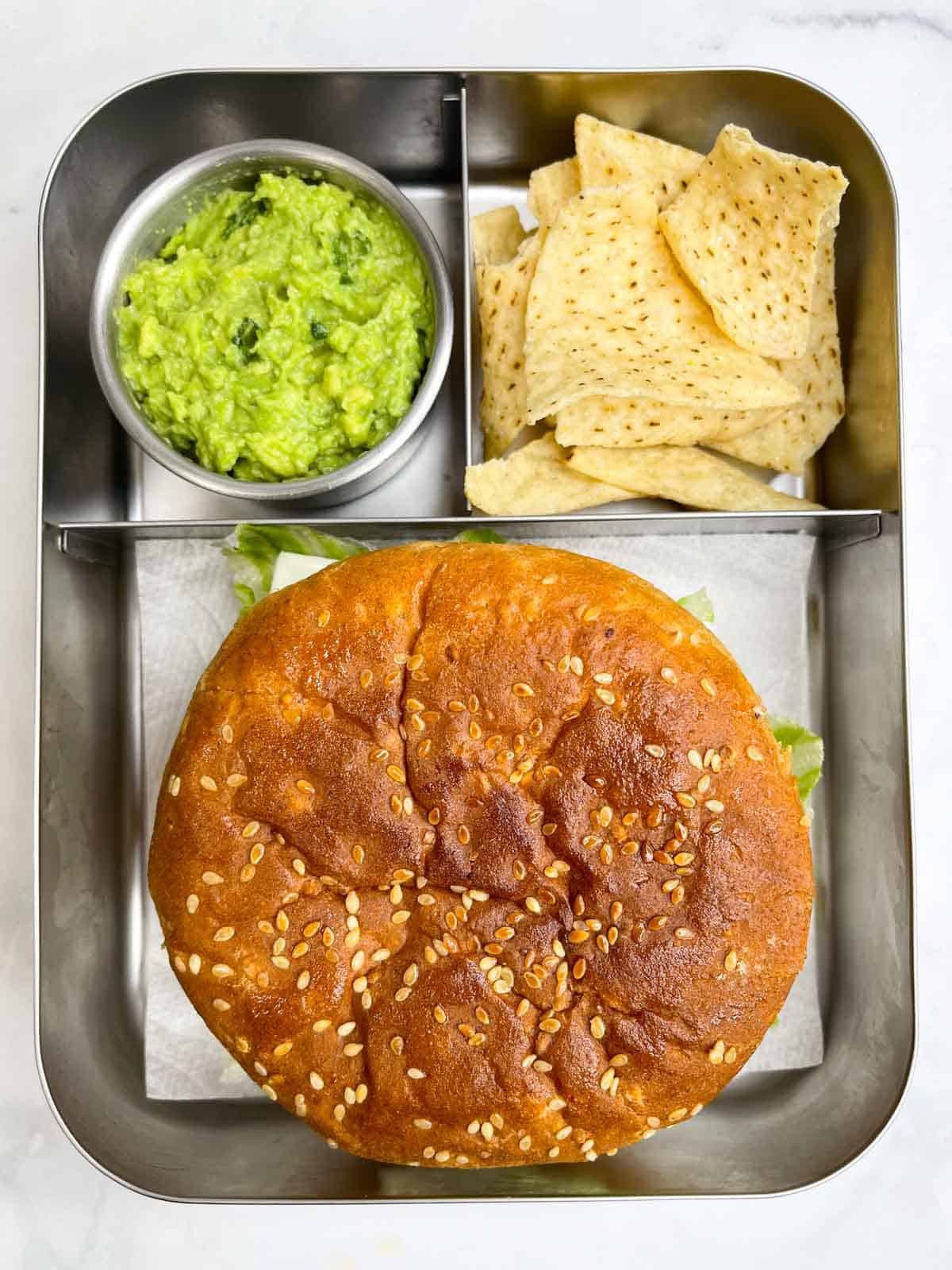 veggie burger with chips and guacamole in bento steel lunch box.