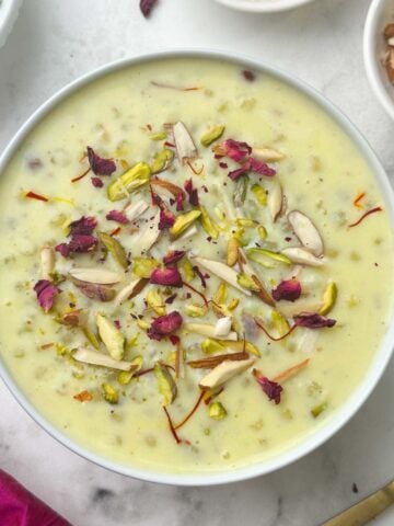 sabudana kheer (indian tapioca pudding) served in a bowl garnished with rose petals and nuts and spoon on the side