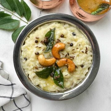 instant pot ven pongal served in a steel bowl garnished with roasted cashews and tempering with coconut chutney and sambar on the side