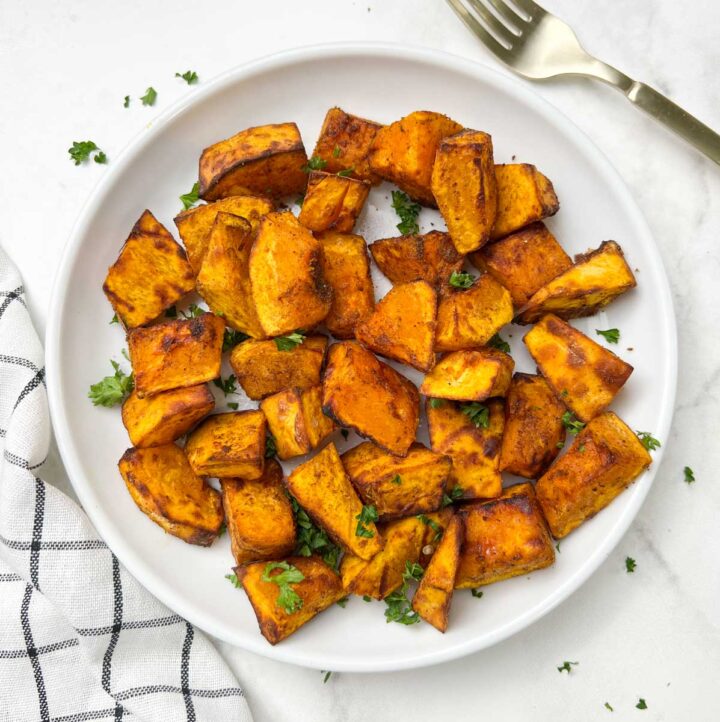 air fryer roasted pumpkin served on a white plate garnished with parsley and fork on the side