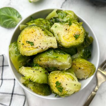 steamed and seasoned instant pot brussels sprouts served in a white bowl with fork on the side