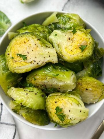 steamed and seasoned instant pot brussels sprouts served in a white bowl with fork on the side