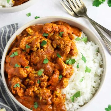 cauliflower tikka masala served with rice, garnished with coriander leaves and forks on the side.