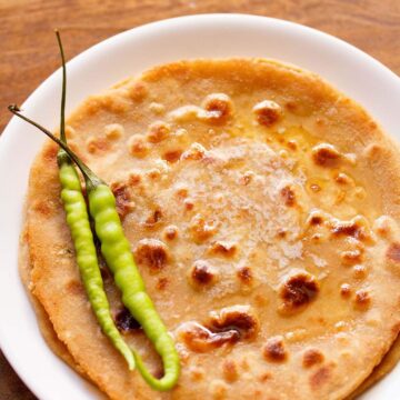 Gobi paratha served on a plate with butter and green chilies on the top.