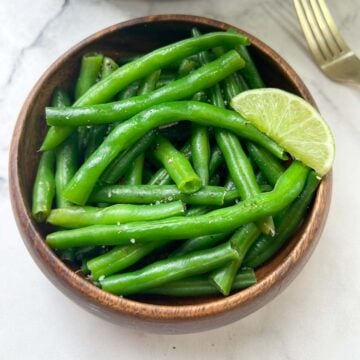 cooked green beans vegetable served in a bowl with lime in top