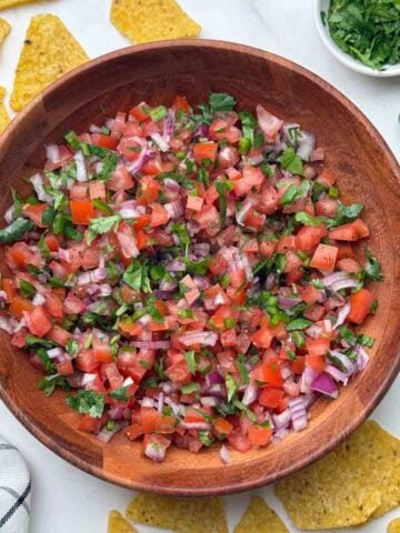 pico de gallo served in a wooden bowl with side of tortilla chips and coriander.