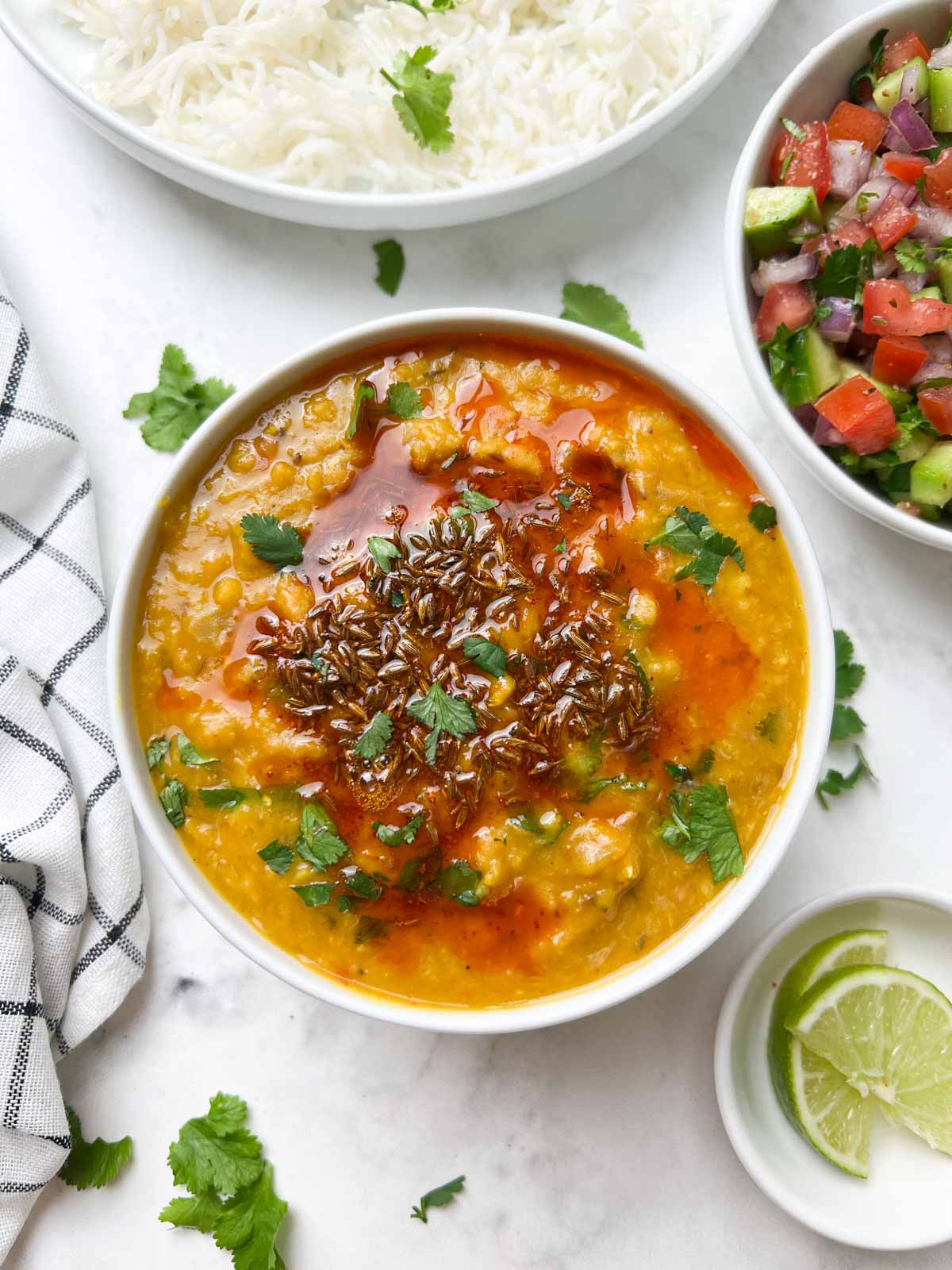 masoor dal(red lentil dal) served in a bowl with tempering on the top with side of salad and lime wedges