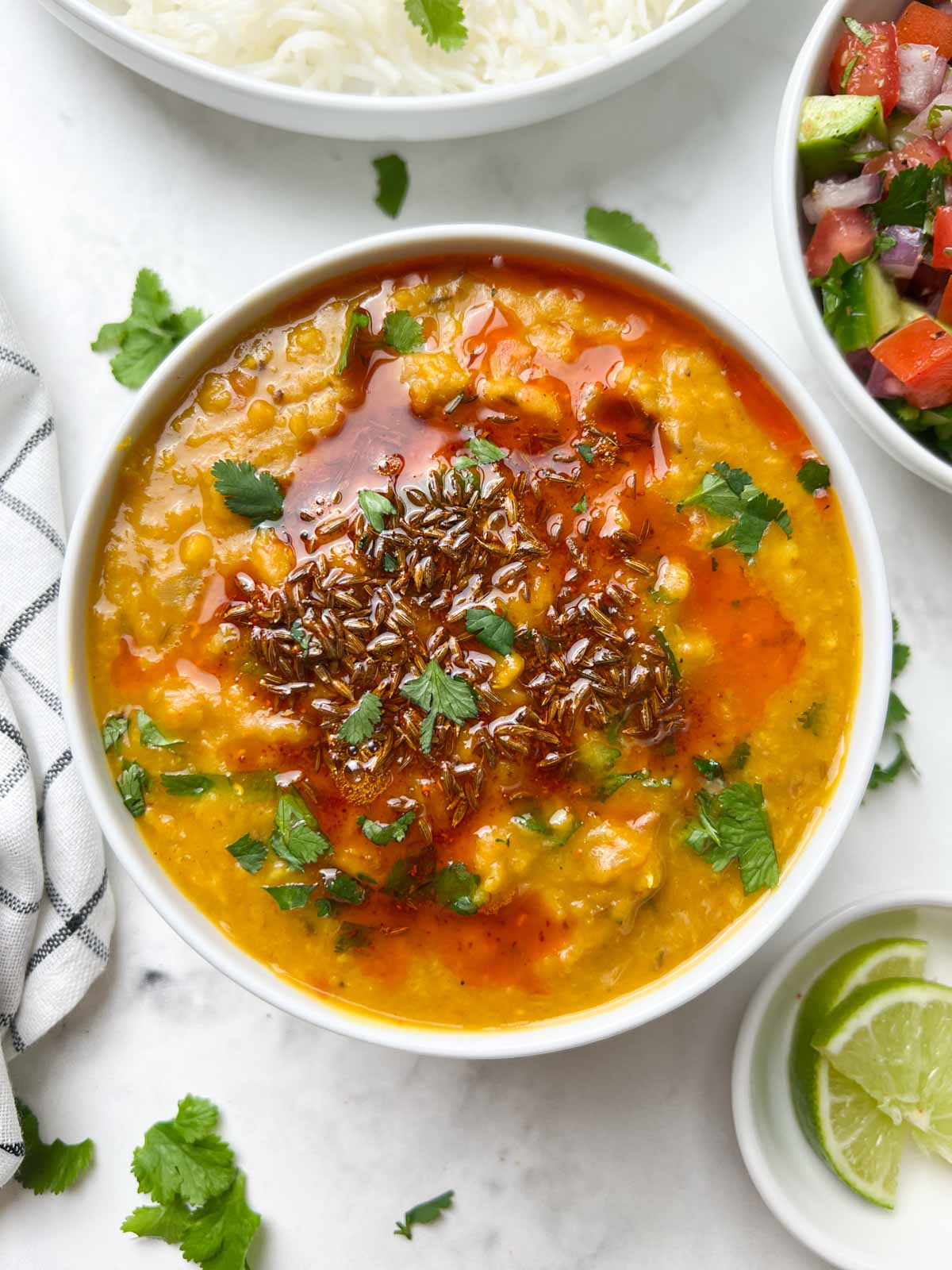 masoor dal(red lentil dal) served in a bowl with tempering on the top with side of salad and lime wedges