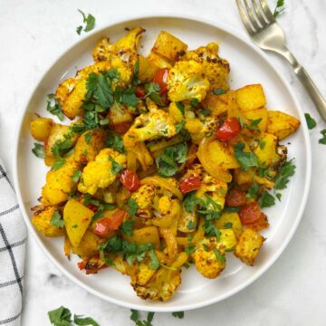 air fryer aloo gobi served on a plate garnished with cilantro and fork on the side